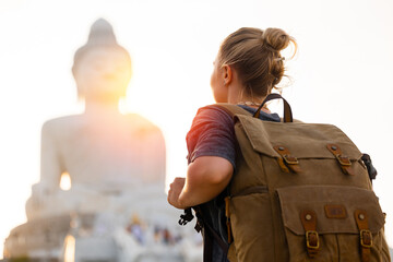 Traveler with backpack admiring golden buddha on Phuket Thailand at sunset