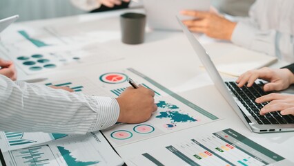 A professional team collaborates during a business meeting, analyzing financial reports and data charts with technology and documents scattered across a desk. SACTR