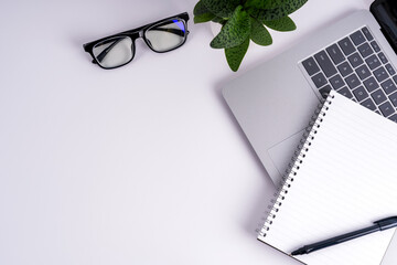 Office desk with eyeglasses, notepad, plant and pen on white background