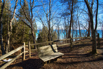 Winter day landscape of an empty bench and wooden fence on a forested bluff with Lake Michigan visible in the distance near Grafton, Wisconsin.