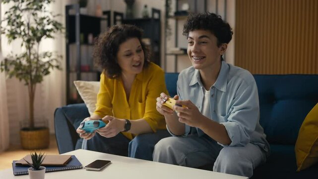 Excited mother and her teen son playing a video game, son celebrating victory