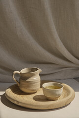 The image showcases two pieces of clay teacups: a handleless bowl-like cup and a small, pitcher-shaped cup reminiscent of a traditional Ukrainian gletchyk. Both are placed on a wooden tray, which