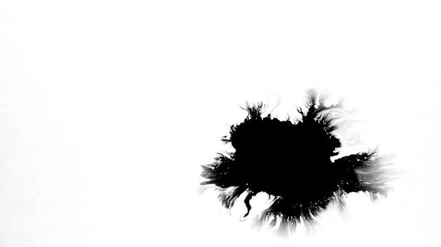 Spraying black paint on a white background. Spray of ink over the white surface. Black watercolor paint spraying. Particles of black paint scatter on white paper. Close up.