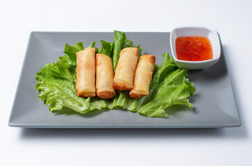 traditional Chinese spring rolls served on a plate with spicy sauce on a white background