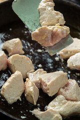 Chicken fillet pieces are fried in a frying pan in oil and turned over with a spatula
