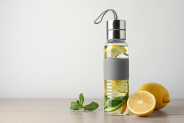Lemon water with mint in bottle on wooden table, space for text