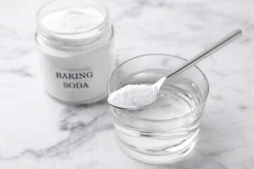Glass of water and baking soda on white marble table, selective focus