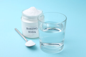 Glass of water and baking soda on light blue background, selective focus