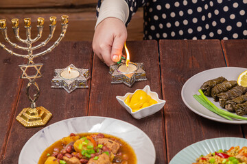 A Jewish woman's hand lights candles on Shabbat in candlesticks with a Star