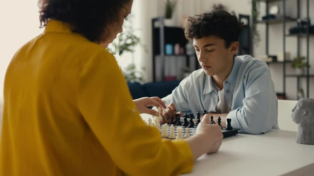 Teenage son playing chess with his mother, family time with a classic board game