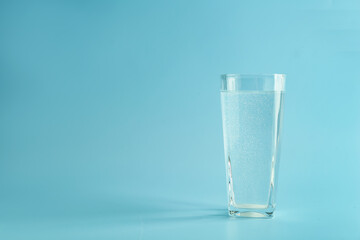 Soda water in glass on light blue background, space for text