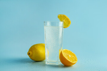Soda water in glass and fresh lemons on light blue background