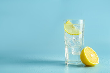 Soda water with lemon and ice cubes in glass on light blue background, space for text