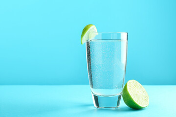 Soda water with lime in glass on light blue background, space for text