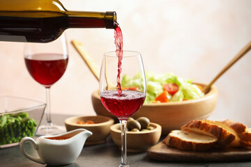 Pouring red wine into glass at grey table with tasty food, closeup