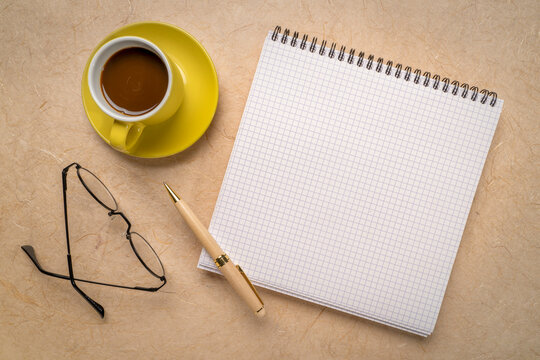 blank spiral notebook with grid paper, flat lay with coffee and reading glasses on textured art paper