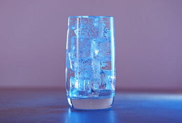 Glass of refreshing soda water with ice cubes in blue light on table, closeup