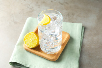 Refreshing soda water with ice cubes in glass and cut lemon on grey textured table, closeup