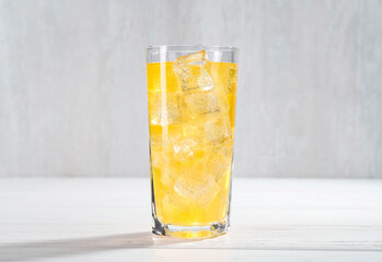 Sweet soda water with ice cubes in glass on white wooden table