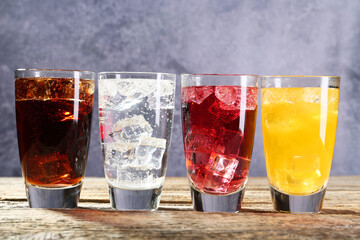 Soda water of different flavors with ice cubes in glasses on wooden table