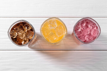 Soda water of different flavors with ice cubes in glasses on white wooden table, top view