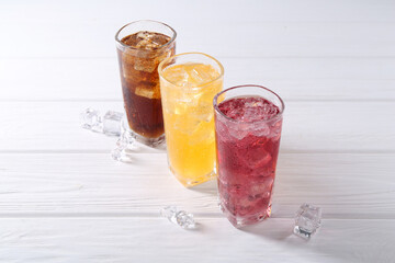 Soda water of different flavors in glasses with ice cubes on white wooden table