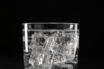 Refreshing soda water with ice cubes in glass on black background, closeup