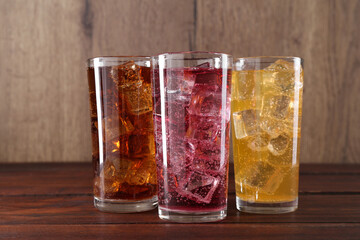 Refreshing soda water of different flavors with ice cubes in glasses on wooden table