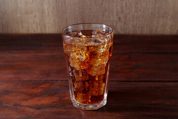 Sweet soda water with ice cubes in glass on wooden table