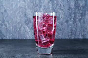 Sweet soda water with ice cubes in glass on grey table