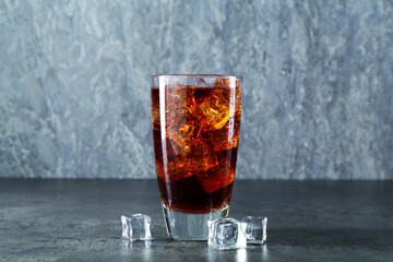Sweet soda water in glass with ice cubes on grey table