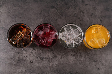 Sweet soda water of different flavors with ice cubes in glasses on grey table, flat lay