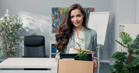 Attractive beautiful smiling brunette in shirt stands in front of desk in company office in hands...