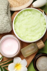 Different body care products, plumeria flowers and twig on green background, flat lay