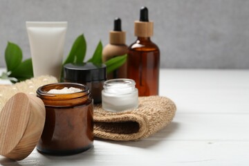 Different body care products and green leaves on white wooden table, closeup. Space for text