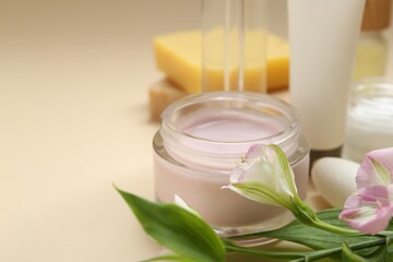 Different body care products, flowers and leaves on beige background, closeup. Space for text