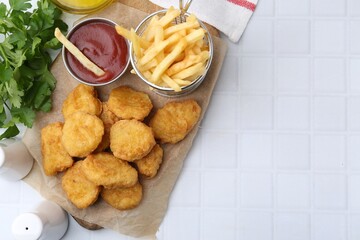 Tasty chicken nuggets, potato fries and ketchup on white tiled table, flat lay. Space for text
