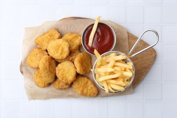 Tasty chicken nuggets, potato fries and ketchup on white tiled table, top view