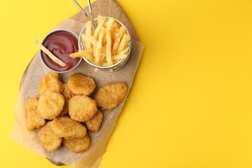 Tasty chicken nuggets, potato fries and sauce on yellow background, top view. Space for text