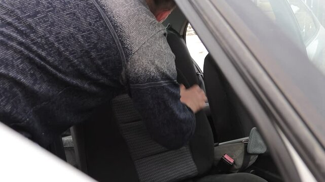 A male craftsman with an injured arm puts a seat cover on a car. The left arm is deformed. The concept of equal opportunities for the disabled.