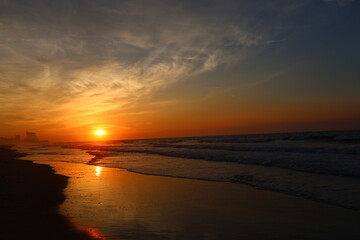 A breathtaking sunset over the ocean, casting golden hues across the sky and reflecting beautifully on the wet sand.