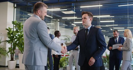 Positive middle aged boss, businessman is shaking hands with an happy male employee during a work meeting in the office. This gesture symbolizes teamwork, partnership, and a successful deal.