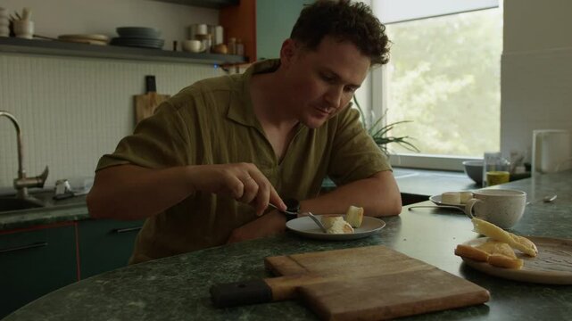 A young man is eating a cheese dessert in the kitchen at home.