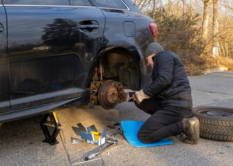 Man changing brake pads on car outdoors. Vehicle is lifted with  jack. Car repair and maintenance...