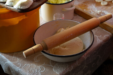 A wooden rolling pin rests in a bowl of dough, on a table with various kitchen utensils.