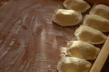 Formed pierogi in a row lie on a wooden board sprinkled with flour.