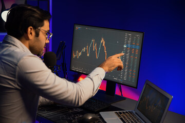 Smart trader businessman concentrating on dynamic stock exchange investment on pc and laptop showing on screen with high profit in searching market at neon light office in dark room night. Surmise.