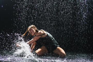 Contemporary woman dancer posing in rain water on black background. Female artist performer dancing with expression. Modern ballerina dancing in darkness. Passion dance in dark. Flexibility balance