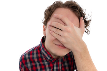 Fototapeta premium A young man in a plaid shirt covering his face with his hand, expressing a playful emotion.