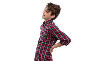 A young man in a plaid shirt smiling and standing with his hand on his hip against a white...